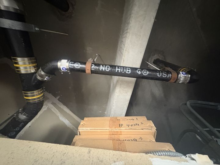 New black no-hub cast iron drain pipe with banded stainless couplings and hangers, installed overhead in a ceiling space