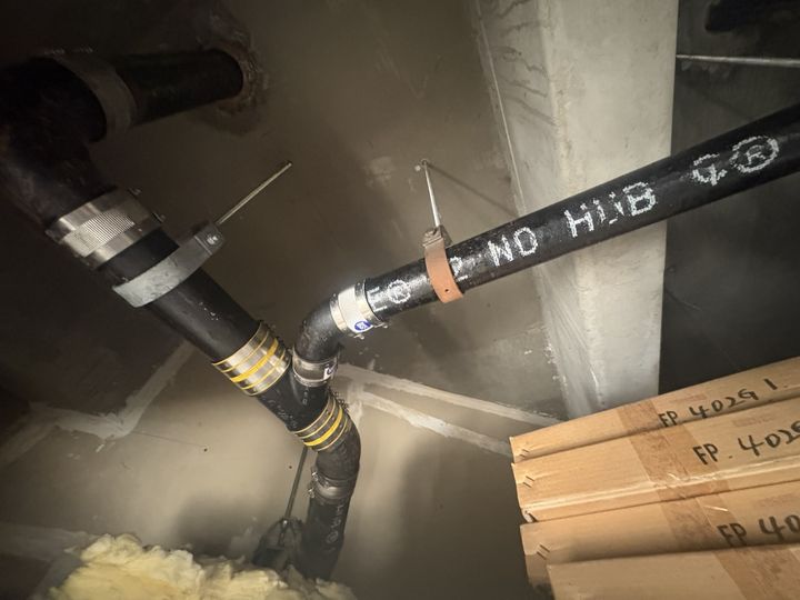 New no-hub cast iron drain pipe joined to existing cast iron with banded couplings, supported by hangers overhead