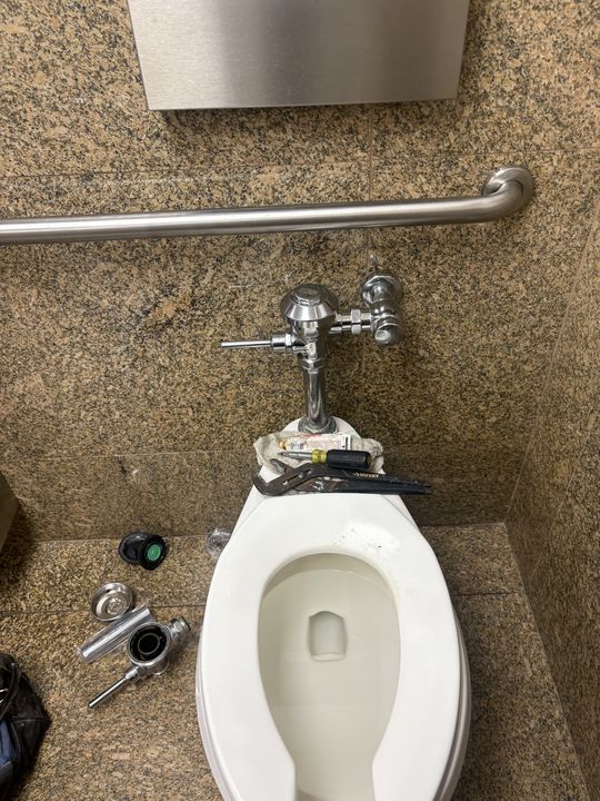Commercial toilet flush valve being rebuilt, with old internal parts and tools laid out